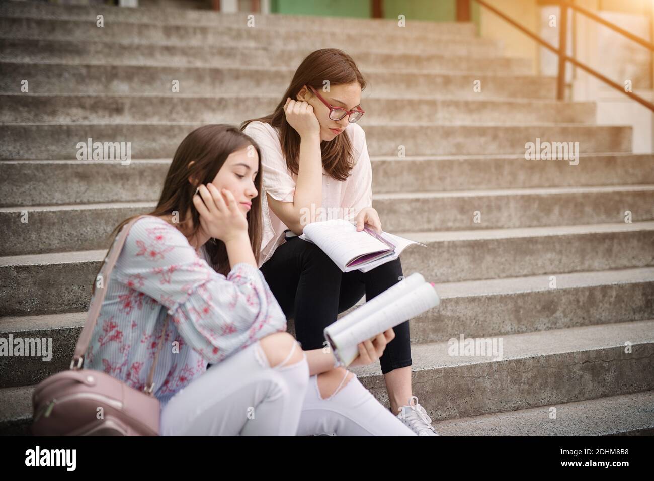 Zwei leider High School Mädchen sitzen auf Treppen außerhalb der Schule und versuchen, Hausaufgaben zu machen. Stockfoto