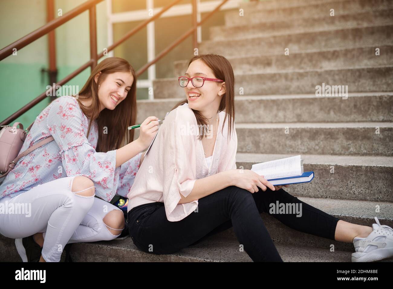 Zwei liebenswert verspielte High School Mädchen machen Hausaufgaben zusammen, während einer von ihnen hält Schulnoten auf der Rückseite eines anderen Mädchens. Stockfoto