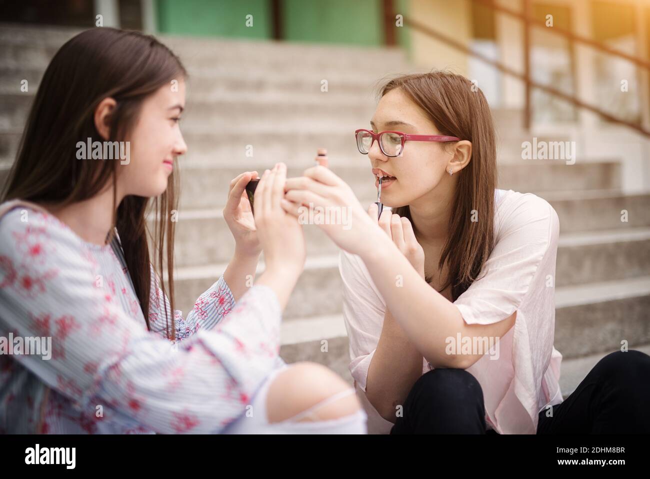 Zwei entzückende charmante High School Mädchen Anwendung Make-up, während auf Treppen außerhalb der Schule sitzen. Stockfoto