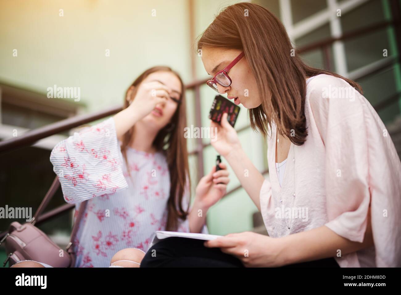 Fleißige intelligente High School Mädchen Schulnoten lesen und auf Treppen außerhalb der Schule sitzen, während ein anderes Mädchen Make-up. Stockfoto