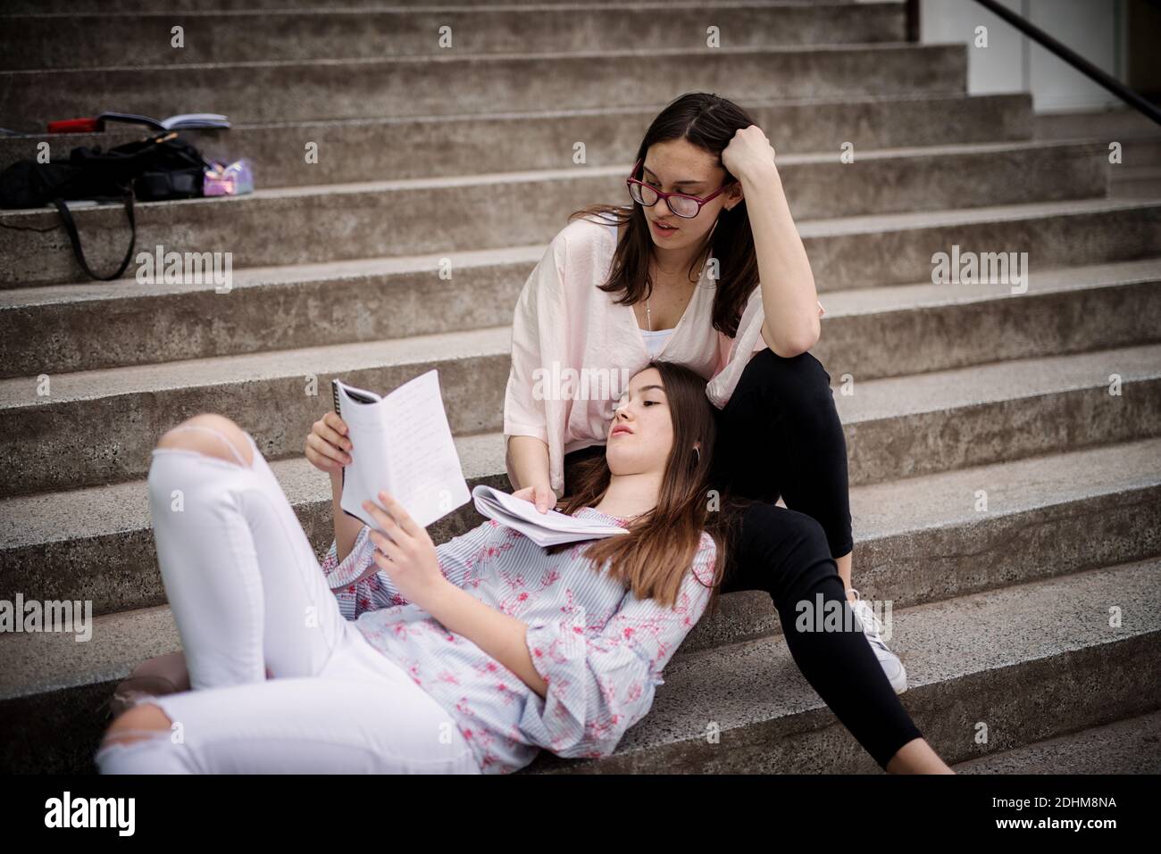 Ziemlich High School Mädchen auf Treppen liegend gegen Schulkamerad Mädchen Bein lehnen und gemeinsam Schulnoten lesen. Stockfoto