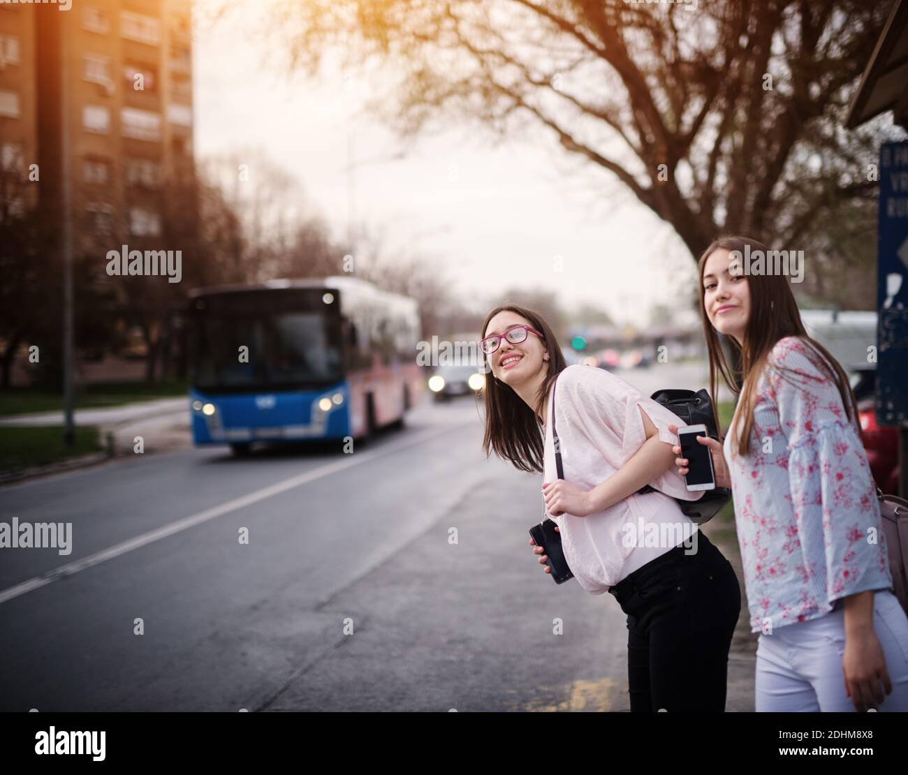 Zwei entzückende niedliche High School Mädchen warten auf einen Bus mit Rucksäcken auf der Bushaltestelle. Stockfoto