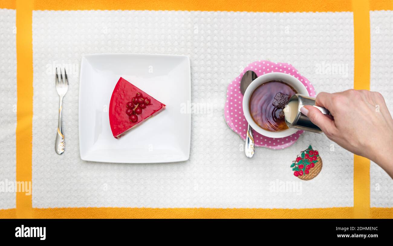 Blick in die Höhe von einem roten Beerenkuchen und einer weiblichen Hand Gießen frische Sahne auf eine Tasse Tee. Stockfoto
