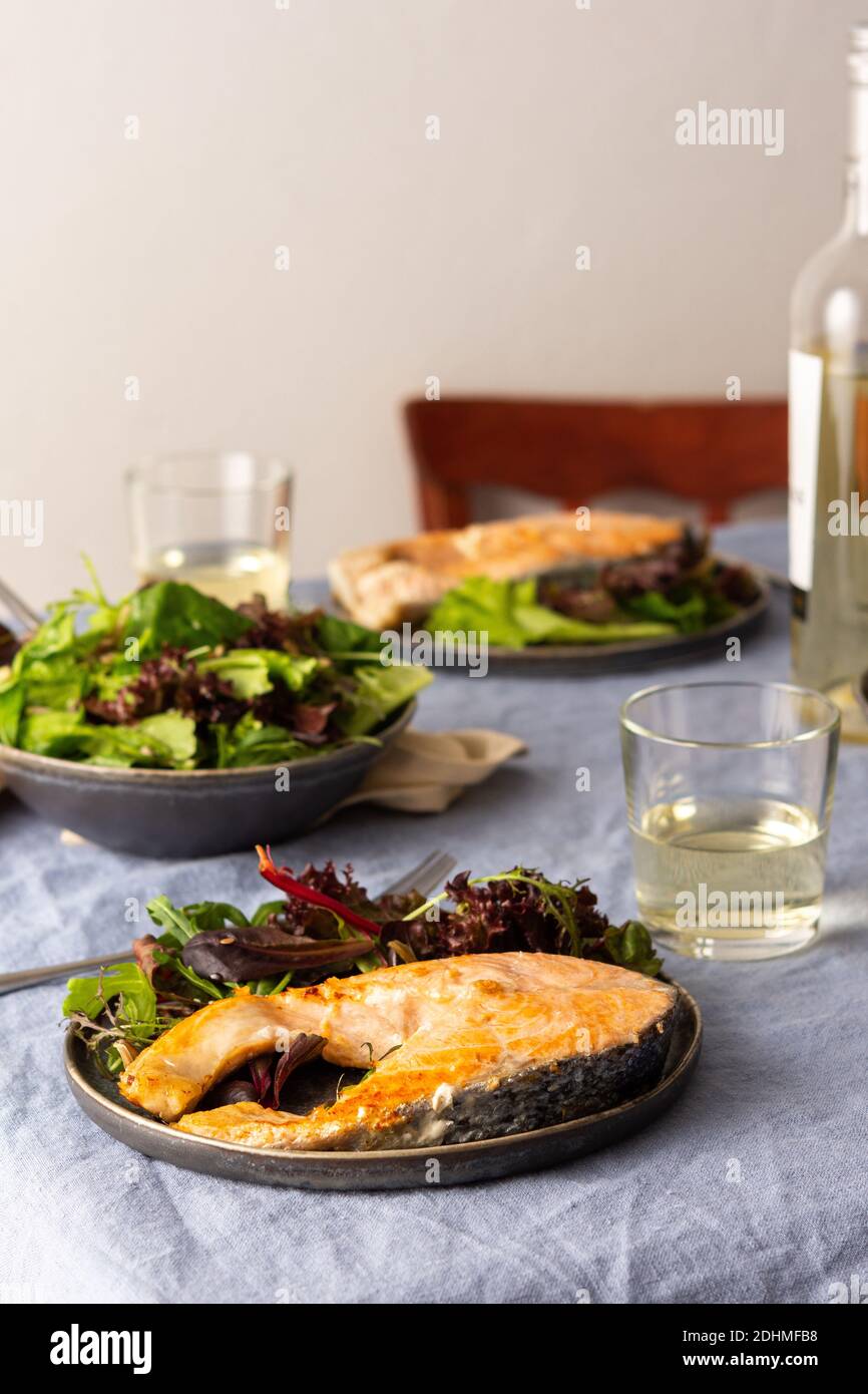 Gebratenes Lachssteak mit Salat auf einem Teller, Weißwein im Glas, leckeres herzhaftes Abendessen oder Mittagessen Stockfoto
