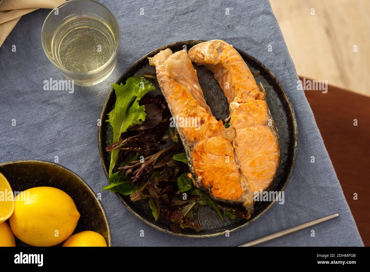 Gebratenes Lachssteak mit Salat auf einem Teller, Weißwein im Glas, leckeres herzhaftes Abendessen oder Mittagessen Stockfoto
