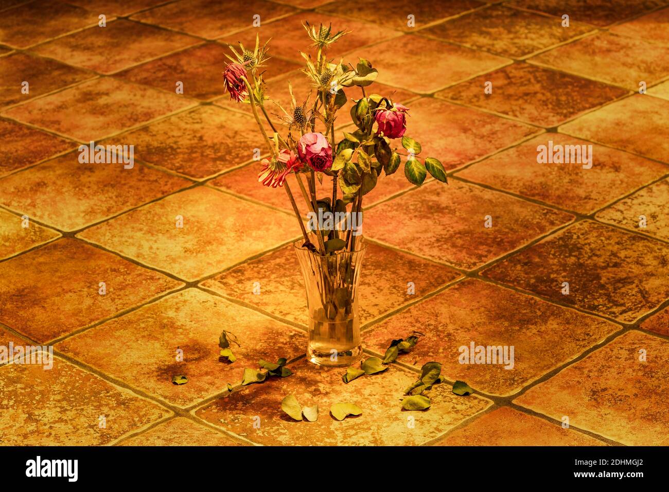 Schöne Nahaufnahme Foto von getrockneten rosa Rosen im Herbst Bouquet steht in transparenter Glasvase auf rustikalen alten Fliesen Boden. Getrocknete Blätter fallen von Stockfoto