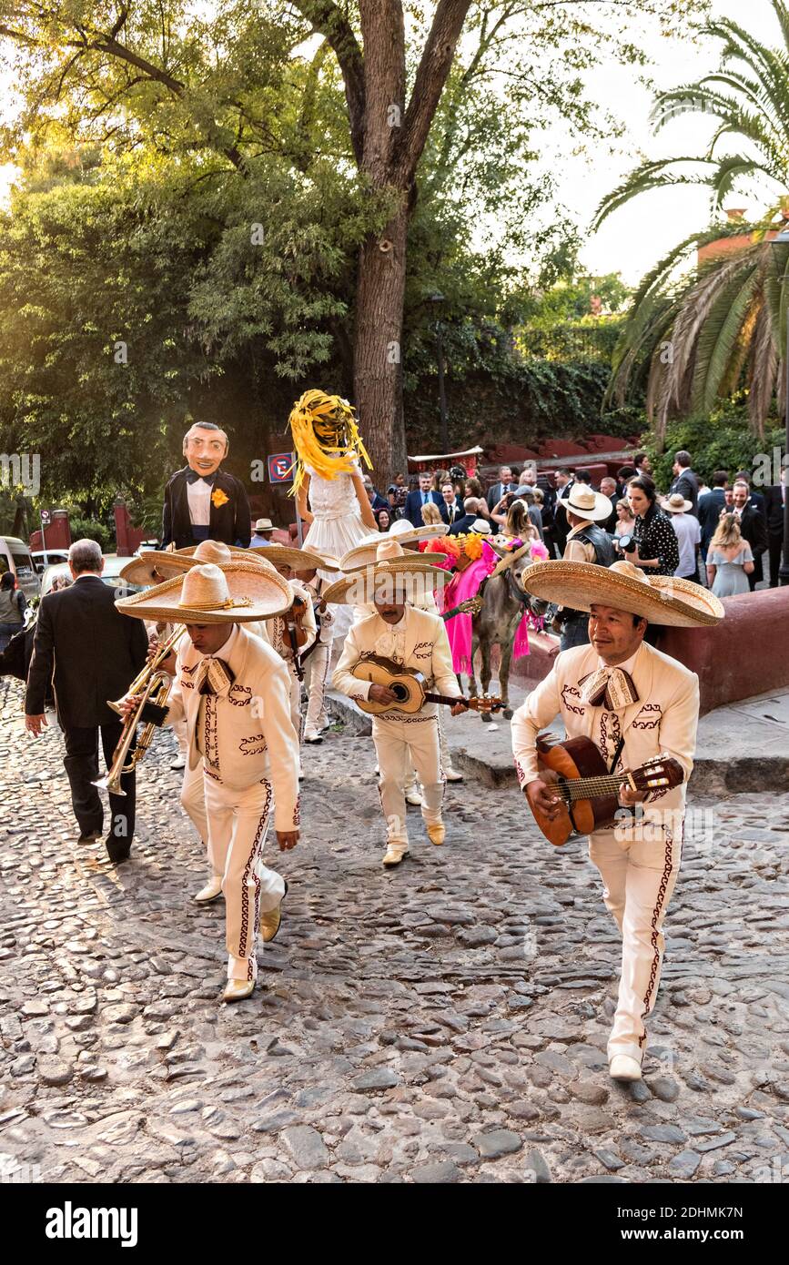 Eine traditionelle mexikanische Mariachi-Band spielt als riesige Puppen namens Mojigangas Tanz während einer Hochzeitsfeier Paraden durch die Straßen San Miguel de Allende, Guanajuato, Mexiko. Stockfoto