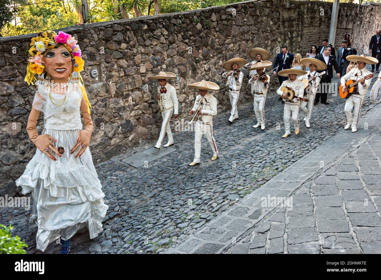 Eine traditionelle mexikanische Mariachi-Band spielt als riesige Puppen namens Mojigangas Tanz während einer Hochzeitsfeier Paraden durch die Straßen San Miguel de Allende, Guanajuato, Mexiko. Stockfoto