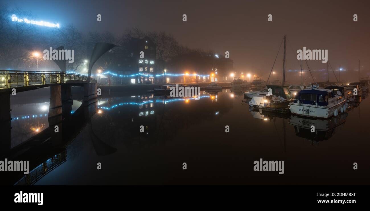 Gebäude und Boote am Hafen sind in einer Herbstnacht im schwimmenden Hafen von Bristol neben der Pero's Bridge in Nebel gehüllt. Stockfoto