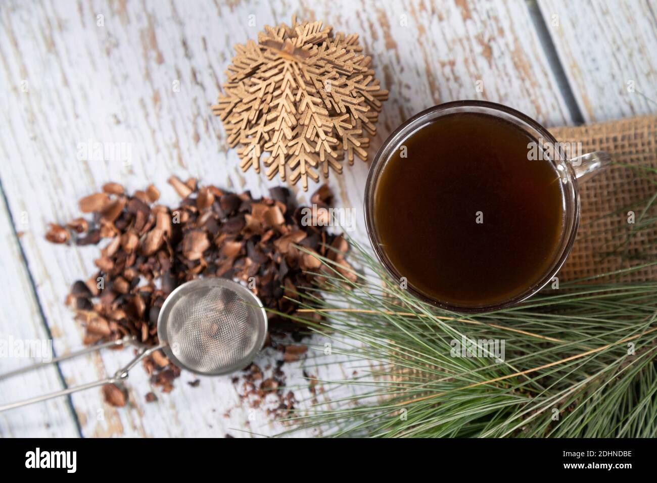 Tasse schwarzen Tee auf weißen Hölzern und Kiefernzweigen - Tee-Infusion - loser schwarzer Tee mit Metallic Ballinfuser Stockfoto
