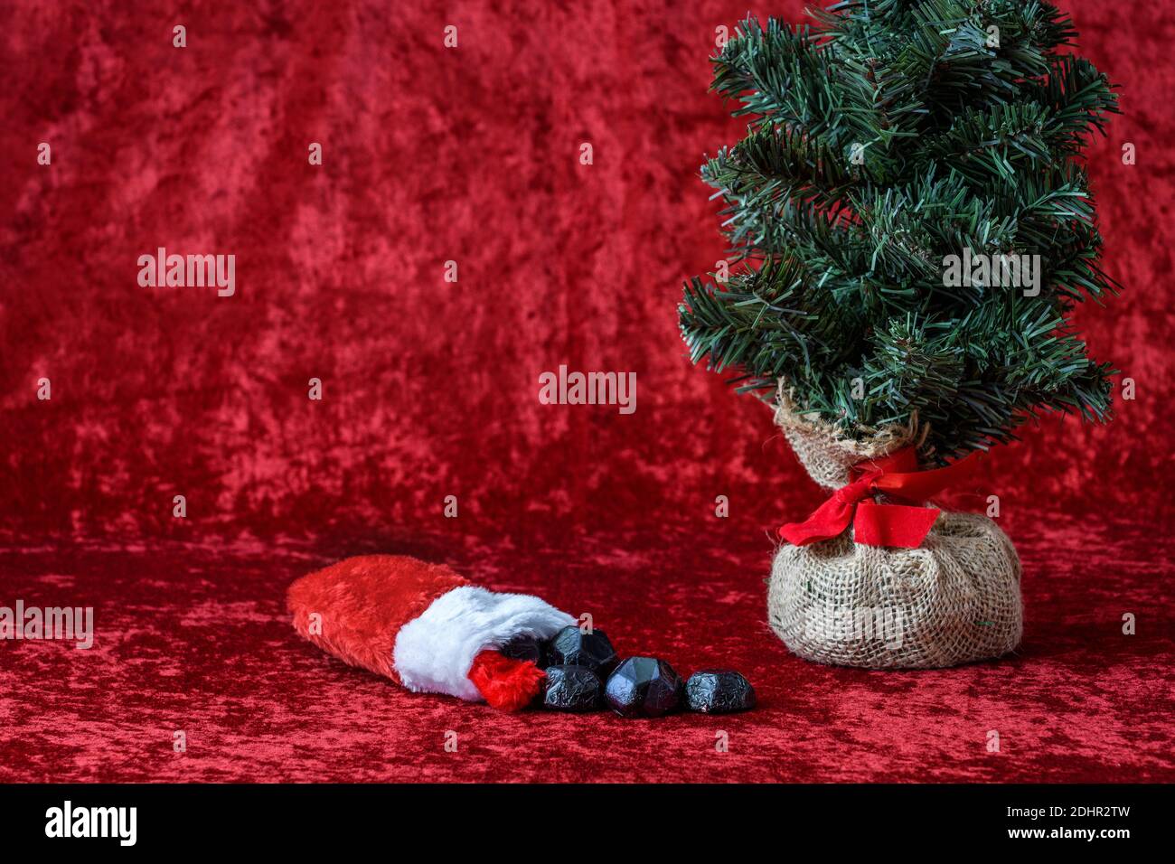 Weihnachtsstrumpf verschüttet Kohle Süßigkeiten, für schlechte Jungen und Mädchen, mit einem Quappen Ball künstlichen Baum, auf einem roten Hintergrund Stockfoto