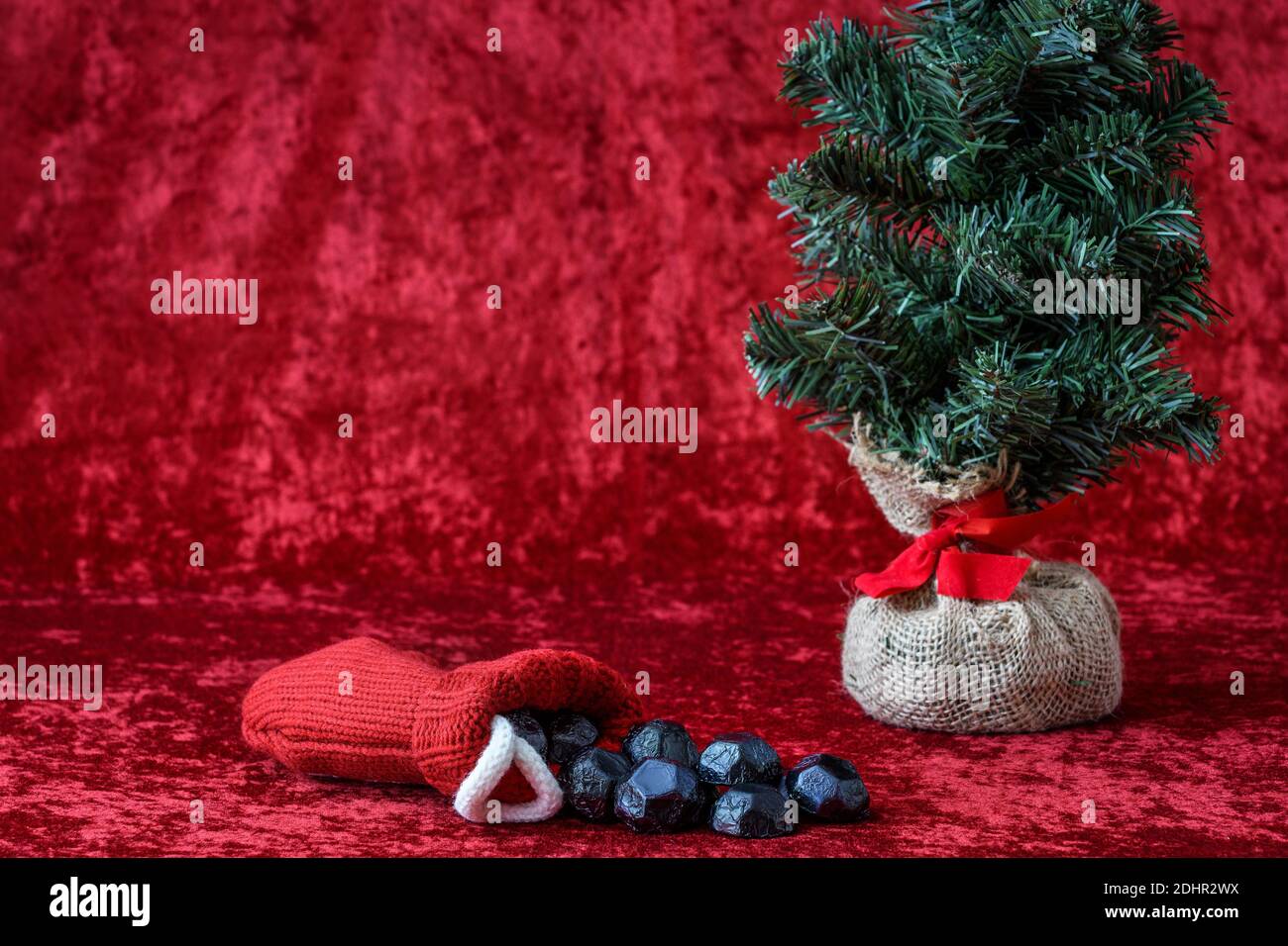 Weihnachtsstrumpf verschüttet Kohle Süßigkeiten, für schlechte Jungen und Mädchen, mit einem Quappen Ball künstlichen Baum, auf einem roten Hintergrund Stockfoto