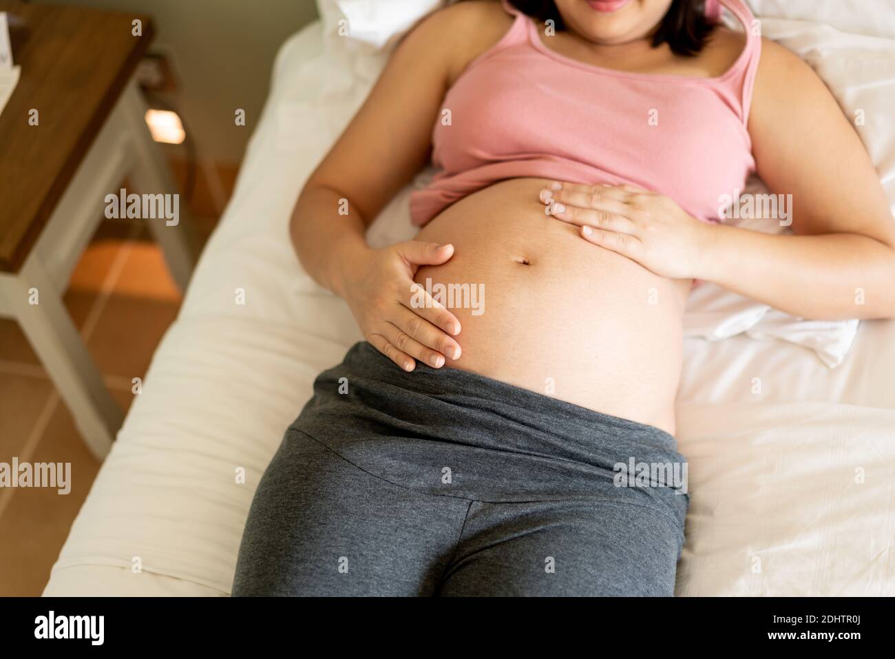 Schwangere Frau, die sich zu Hause glücklich fühlt, während sie sich um ihr Kind kümmert. Die junge schwangere Mutter hält das Baby im schwangeren Bauch. Mutterschaft pränatal Stockfoto