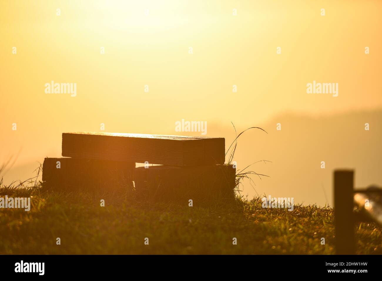 Natur warmes Licht mit Holzbank auf Graswiese mit sonnenaufgang oder Sonnenuntergang im Hintergrund der Berge Stockfoto