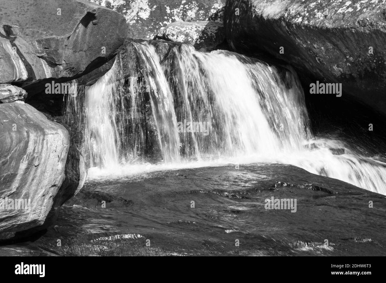 Schwarz-weiße Landschaft in einer sonnigen und fließenden Wasserfalllandschaft mit stark fließendem Wasser. Die Szene wird von einer atemberaubenden Felsformation umhüllt Stockfoto