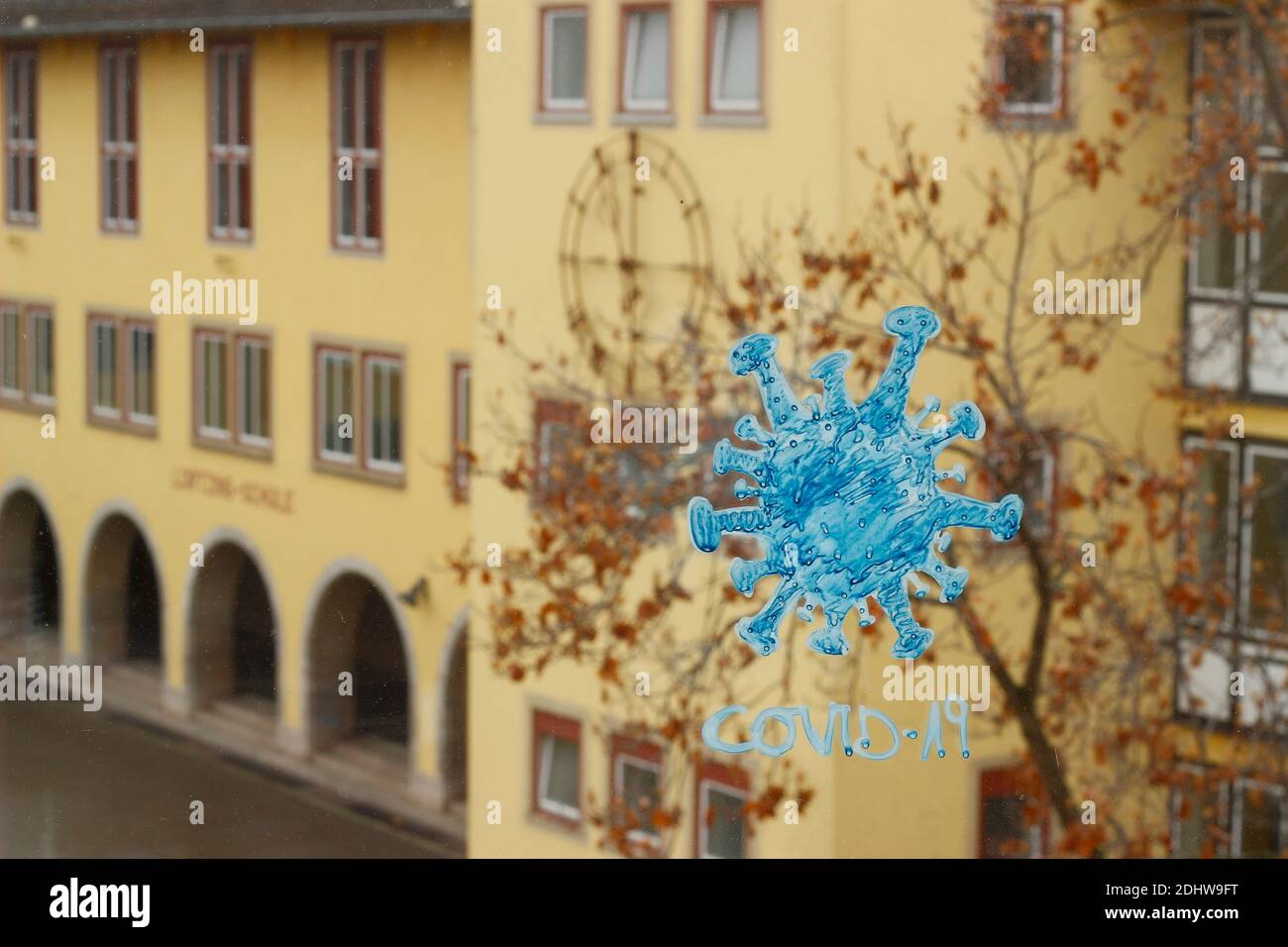 Coronavirus/Covid19 Illustration mit Schule im Hintergrund. Gebäude mit Uhr und Schulhof sichtbar. Stockfoto