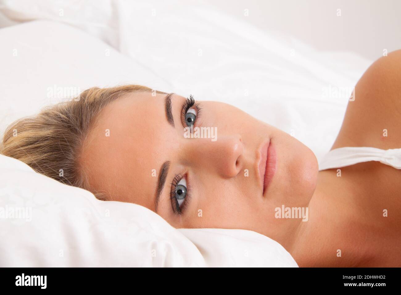 Eine junge blonde Frau liegt wach im Bett. Schlafflos und nachdenklich. Stockfoto
