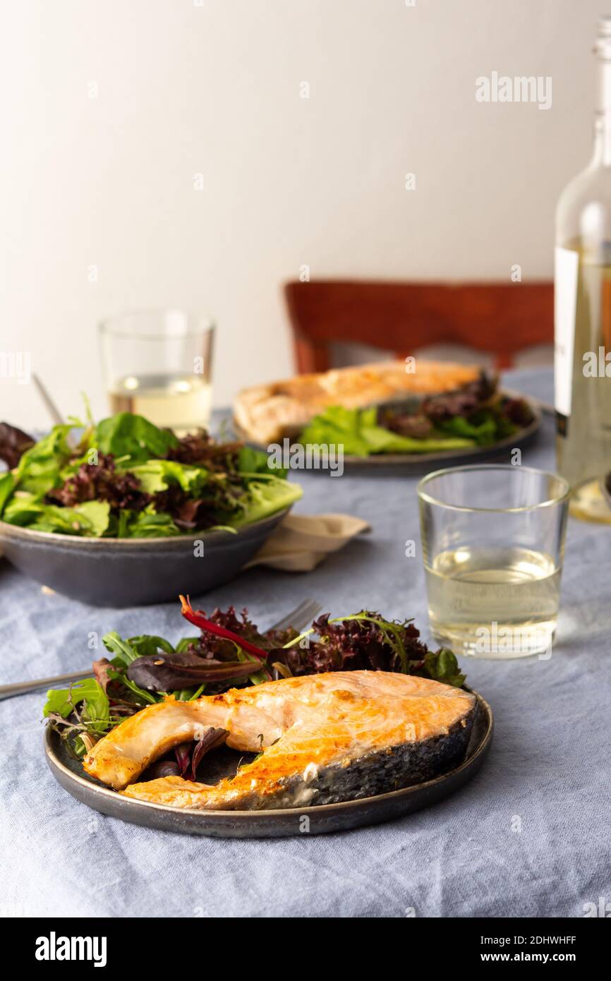Gebratenes Lachssteak mit Salat auf einem Teller, Weißwein im Glas, leckeres herzhaftes Abendessen oder Mittagessen Stockfoto