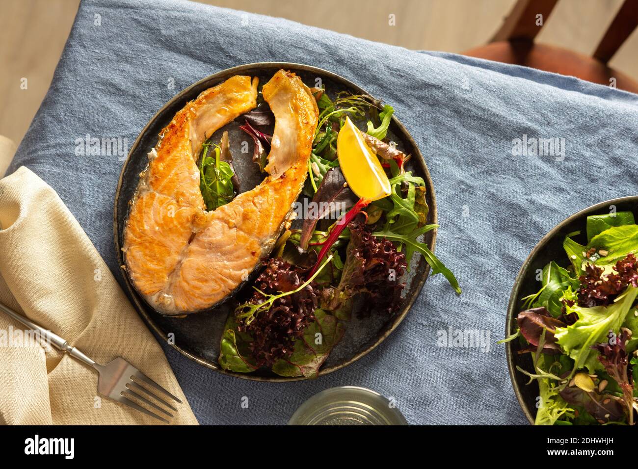 Gebratenes Lachssteak mit Salat auf einem Teller, Weißwein im Glas, leckeres herzhaftes Abendessen oder Mittagessen Stockfoto