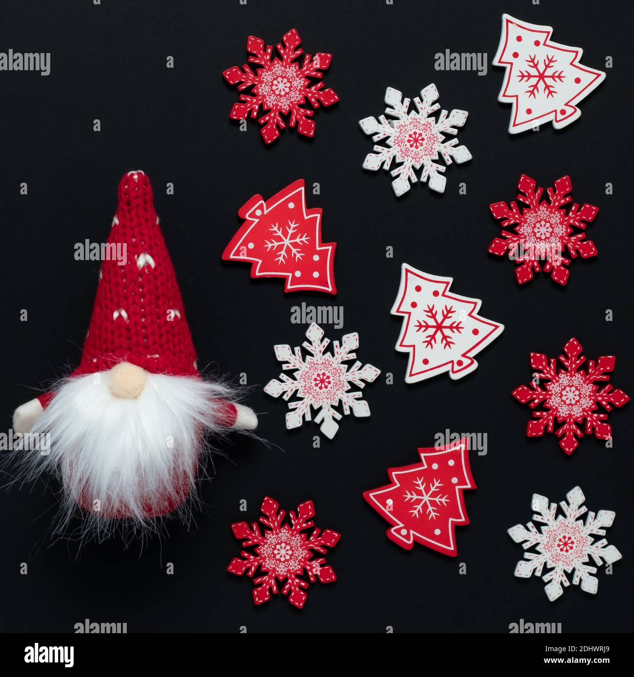 Weihnachtliches Ornament, weiß-rotes Muster auf dunklem Hintergrund. Ein Spielzeug-Gnom in einem Kegelhut mit Bart und farbigen Schneeflocken auf einem schwarzen festlichen New Y Stockfoto