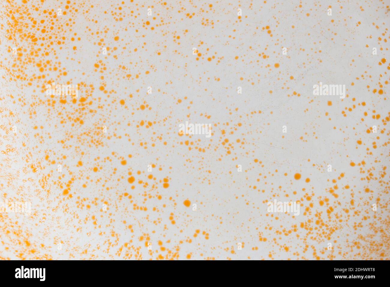 Weiße keramische Oberfläche mit orangefarbenen Farbspritzern gebeizt bildet eine abstrakte Landschaft mit rostiger Textur als Hintergrund. Stockfoto