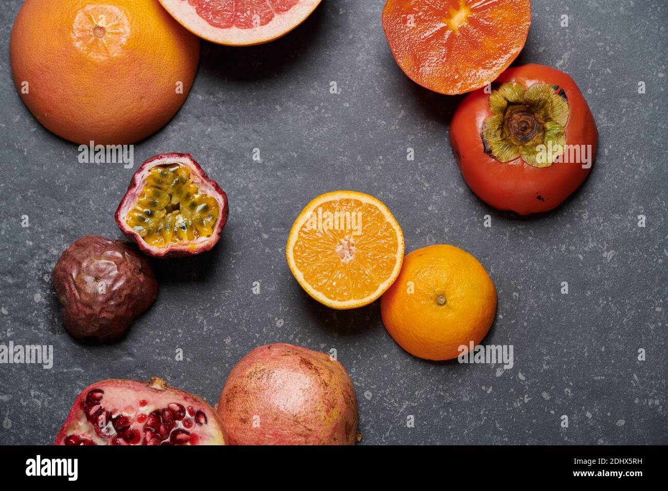 Draufsicht auf Orange mit Grapefruit, Granatapfel, Passionsfrucht und Kaki auf dunkelgrauem Steinhintergrund. Gesunde und frische Früchte zur Steigerung von Vitamin C Stockfoto
