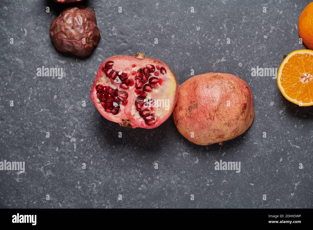 Nahaufnahme des bunten Granatapfels mit Orange und Passionsfrucht auf dunkelgrauem Steinhintergrund. Gesunde und frische Früchte zur Steigerung von Vitamin C Stockfoto