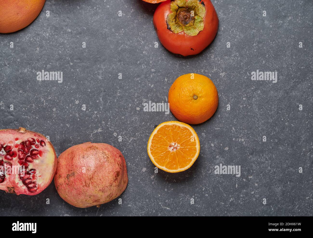 Draufsicht auf Orange, mit Grapefruit, Granatapfel, Passionsfrucht und Kaki auf dunkelgrauem Steinhintergrund im Kreis angeordnet. Gesunde und frische Früchte Stockfoto