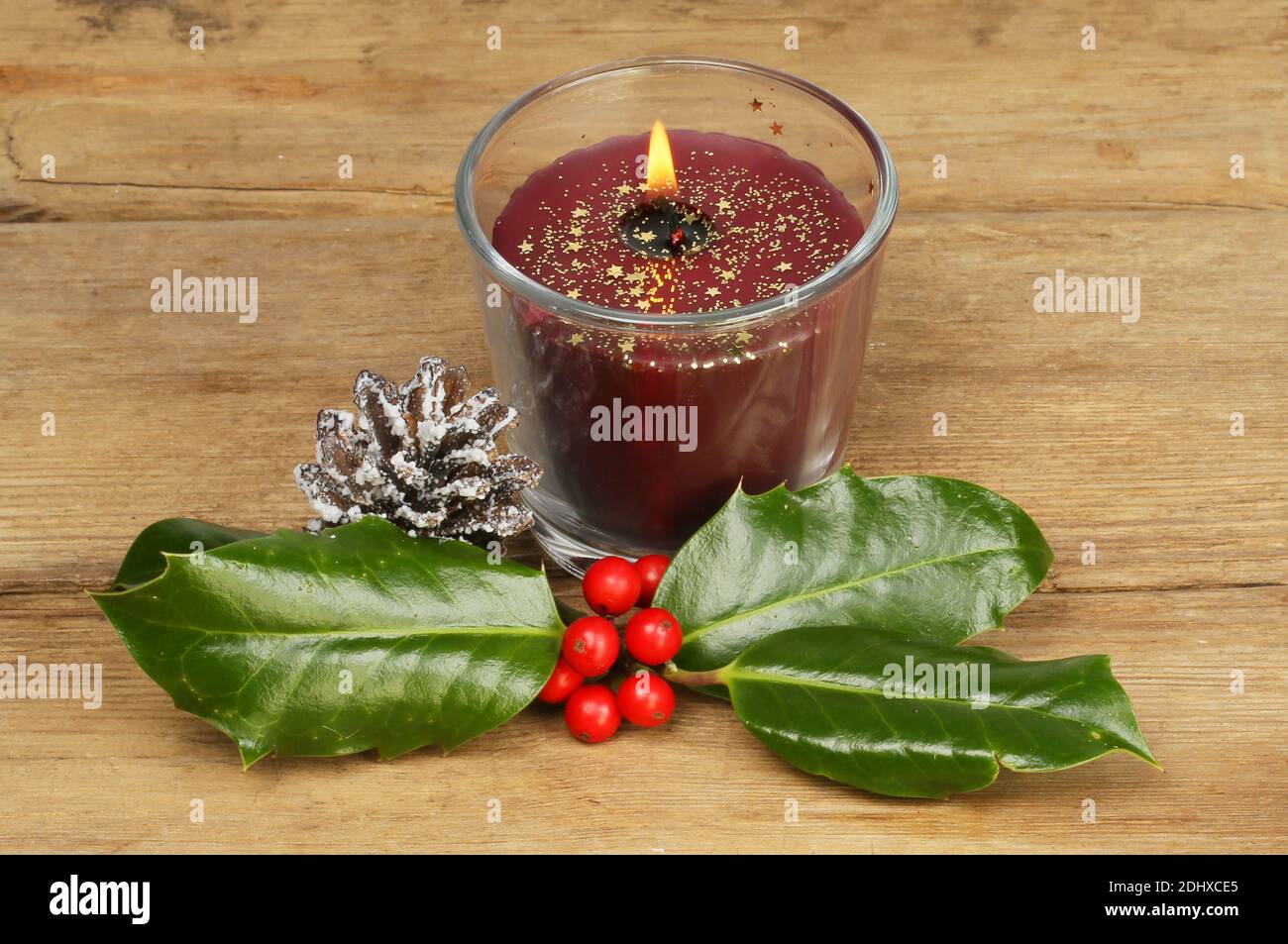 Brennende Weihnachtskerze auf rustikalem Holz mit Stechpalme und ein Schneebedeckter Nadelkrone Stockfoto