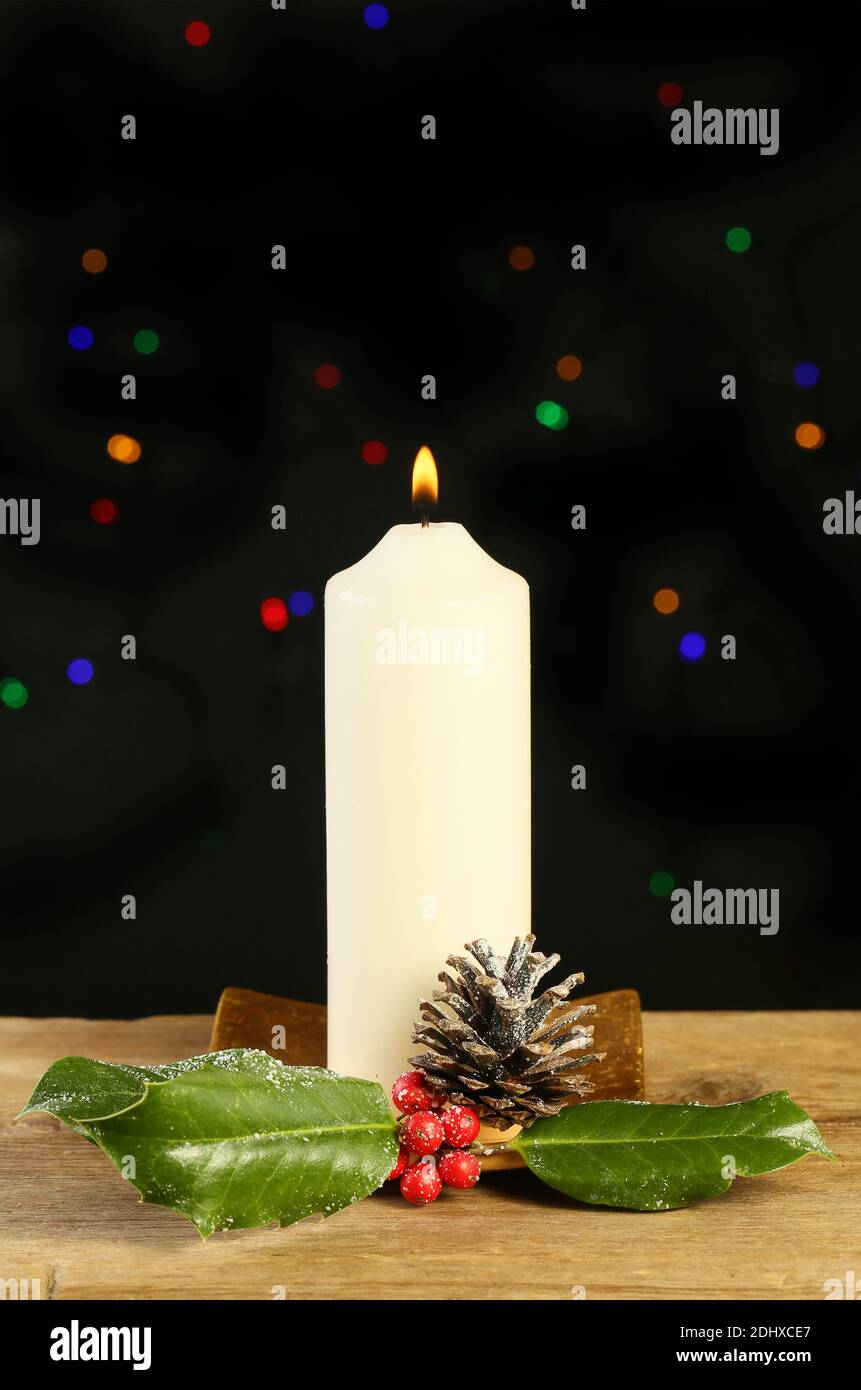 Brennende Kerze mit Stechpalme und einer Pinecone vor einem Hintergrund Von Bokeh Weihnachtsbeleuchtung Stockfoto