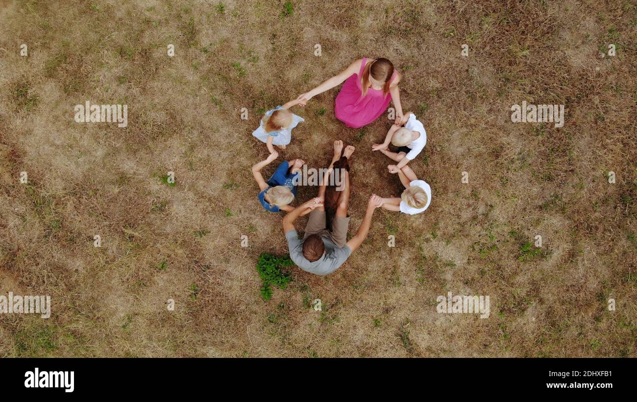 Freundliche Familie winkt mit den Händen, während sie mit einem Hund auf dem Gras sitzt. Blick von der Drohne. Stockfoto