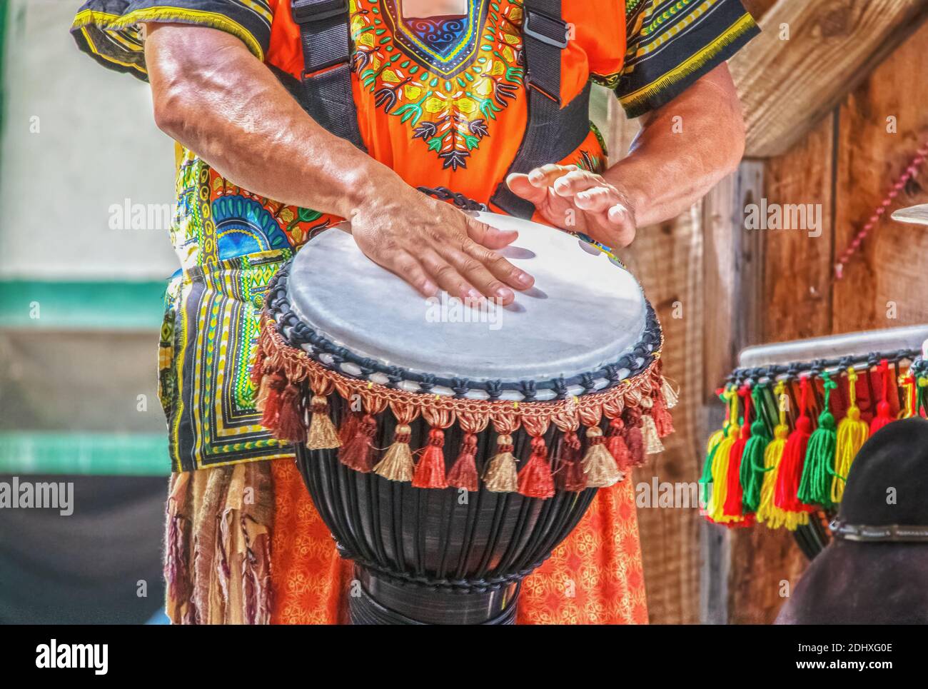 Mann im bunten Kostüm spielt afrikanische ethnische Percussion Trommel mit Quasten vor verschwommenem Hintergrund - abgeschnitten und Bewegungsunschärfe aktiviert Hände Stockfoto