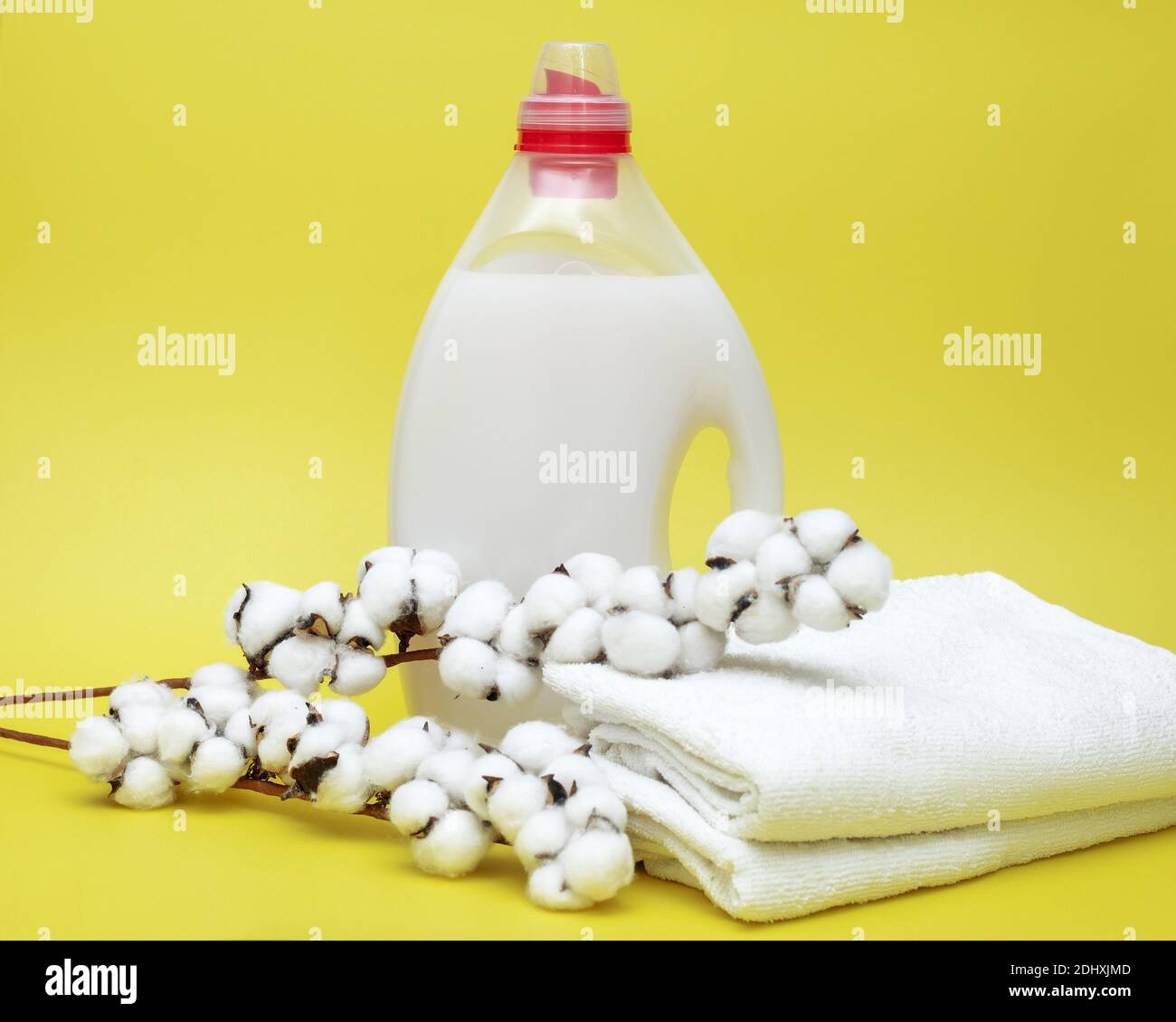 Waschmittel in der Flasche mit Flüssigkeit und Handtücher auf gelbem Hintergrund mit Wattebausch. Waschkonzept Stockfoto