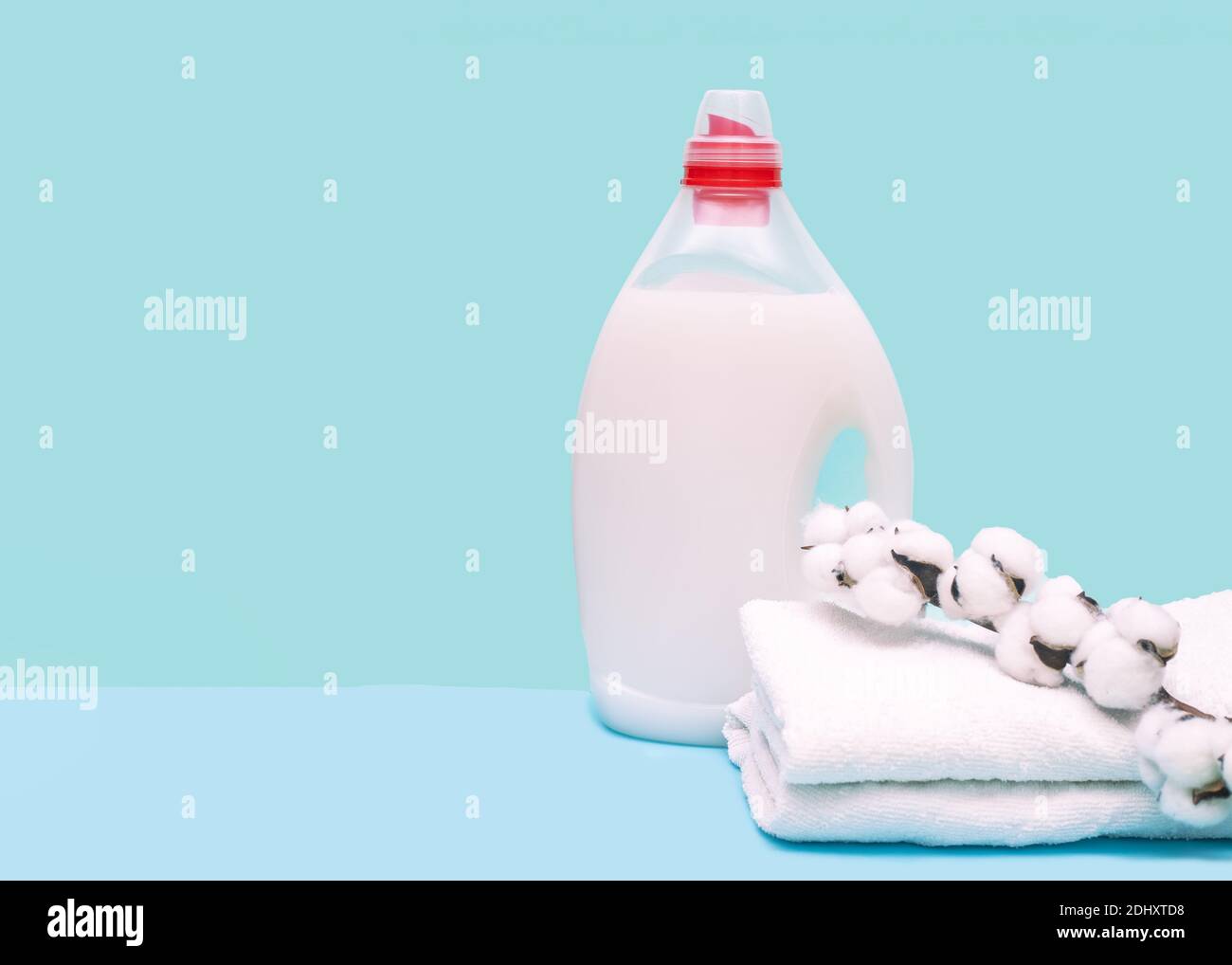 Waschmittel in der Flasche mit Flüssigkeit und Handtücher auf blauem Hintergrund mit Wattebausch. Waschkonzept Stockfoto