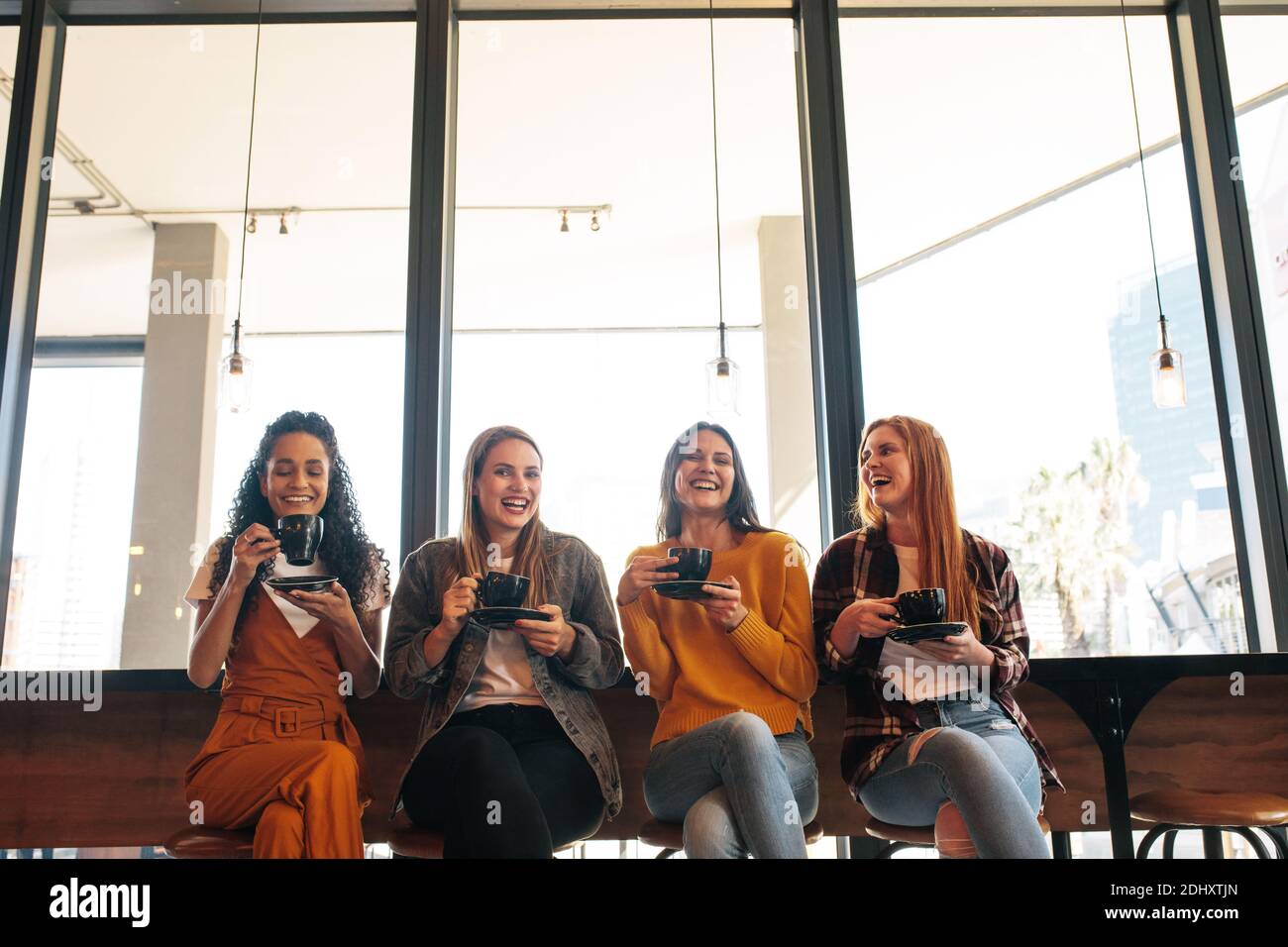 Vier stilvolle junge Frau mit Kaffee in einem Café sitzen. Gruppe von multiethnischen Freundinnen mit Kaffee und verbringen Zeit zusammen bei einem Kaffee sho Stockfoto