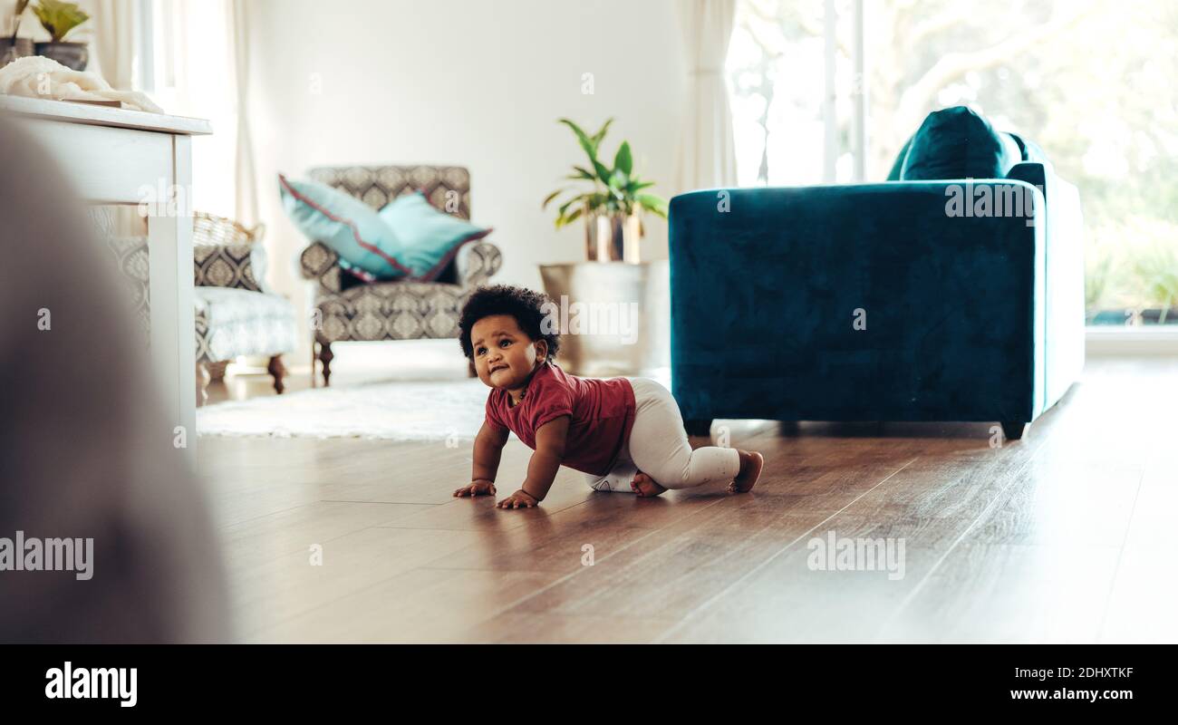 Niedliches Baby kriecht auf dem Boden. Afrikanisches Baby bewegt sich im Wohnzimmer. Stockfoto