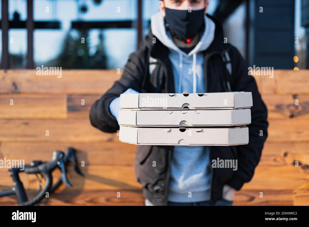Der Lieferer hält Pizzataschachteln in einer ausgestreckten Hand. Lebensmittelzustellung, Fahrradkurier bei der Arbeit, Catering-Konzept zum Mitnehmen Stockfoto
