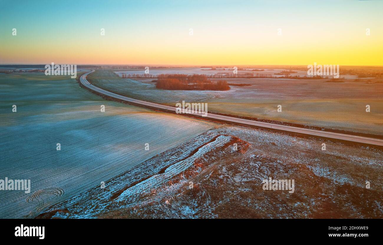 Winter grün Agrarfeld Winterpflanzen unter Schnee-Panorama. Highway Dezember Sonnenuntergang Luftaufnahme. Große Asphaltstraße. Blick auf die Landschaft von oben. Minsk Stockfoto