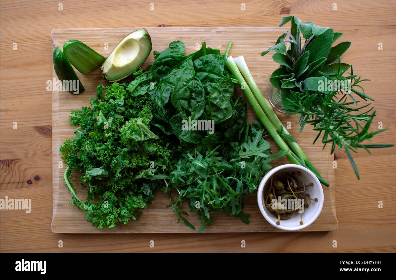 Zutaten für einen frischen und gesunden dunkelgrünen Salat - Grünkohl, Spinat, Rucola, Avocado, Gurke, Kapern, Frühlingszwiebeln Stockfoto