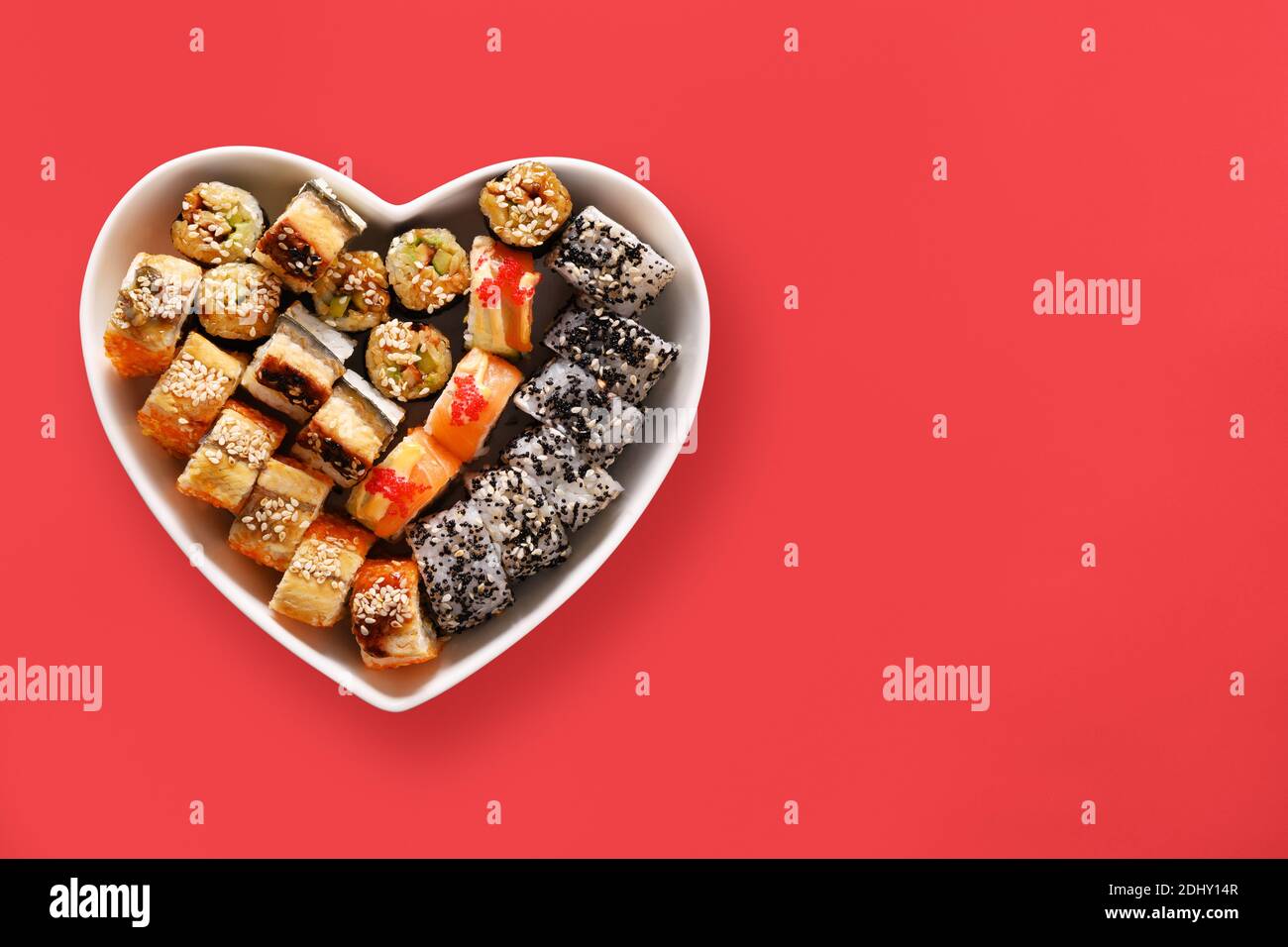 Sushi in Teller als Herz auf rotem Hintergrund. Valentinstag Liebe Konzept. Blick von oben. Leerzeichen für Text. Flach liegend. Stockfoto