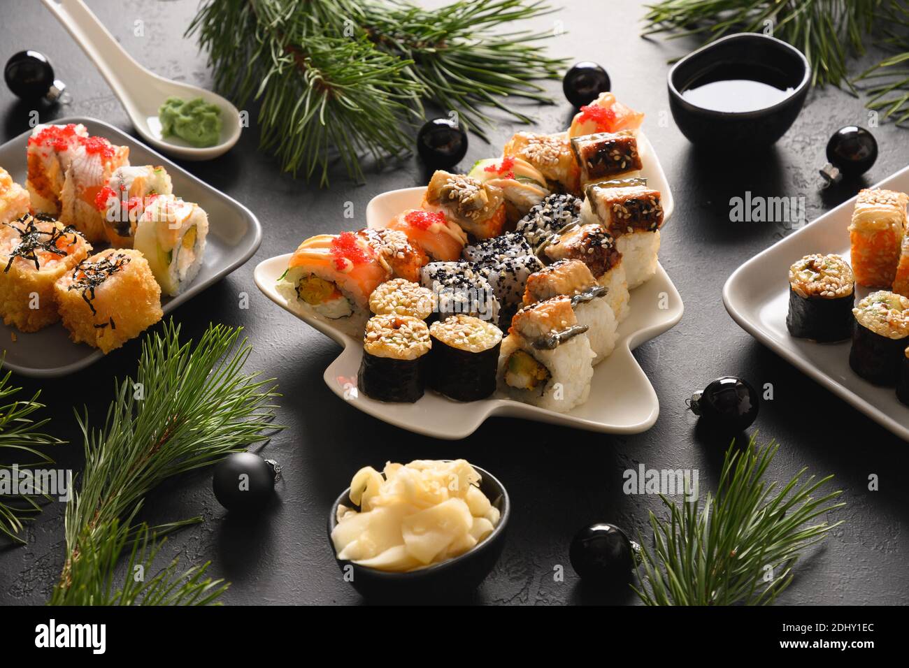 Festliches Weihnachtsessen mit Sushi-Set mit Weihnachtsdekoration auf schwarzem Tisch. Nahaufnahme. Silvesterparty. Stockfoto