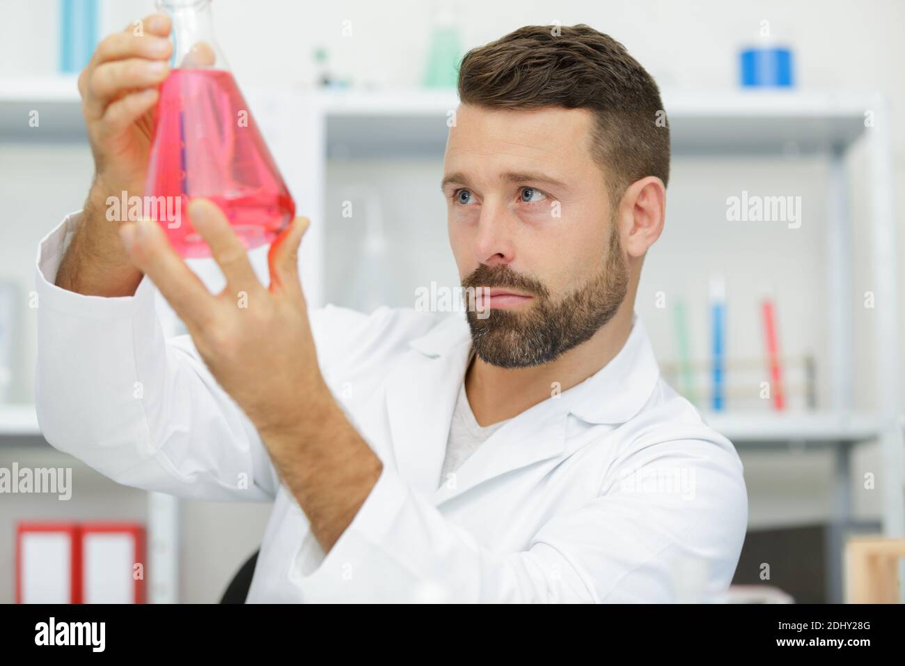 Männlicher Wissenschaftler untersucht rote Flüssigkeit in Glasflasche Stockfoto