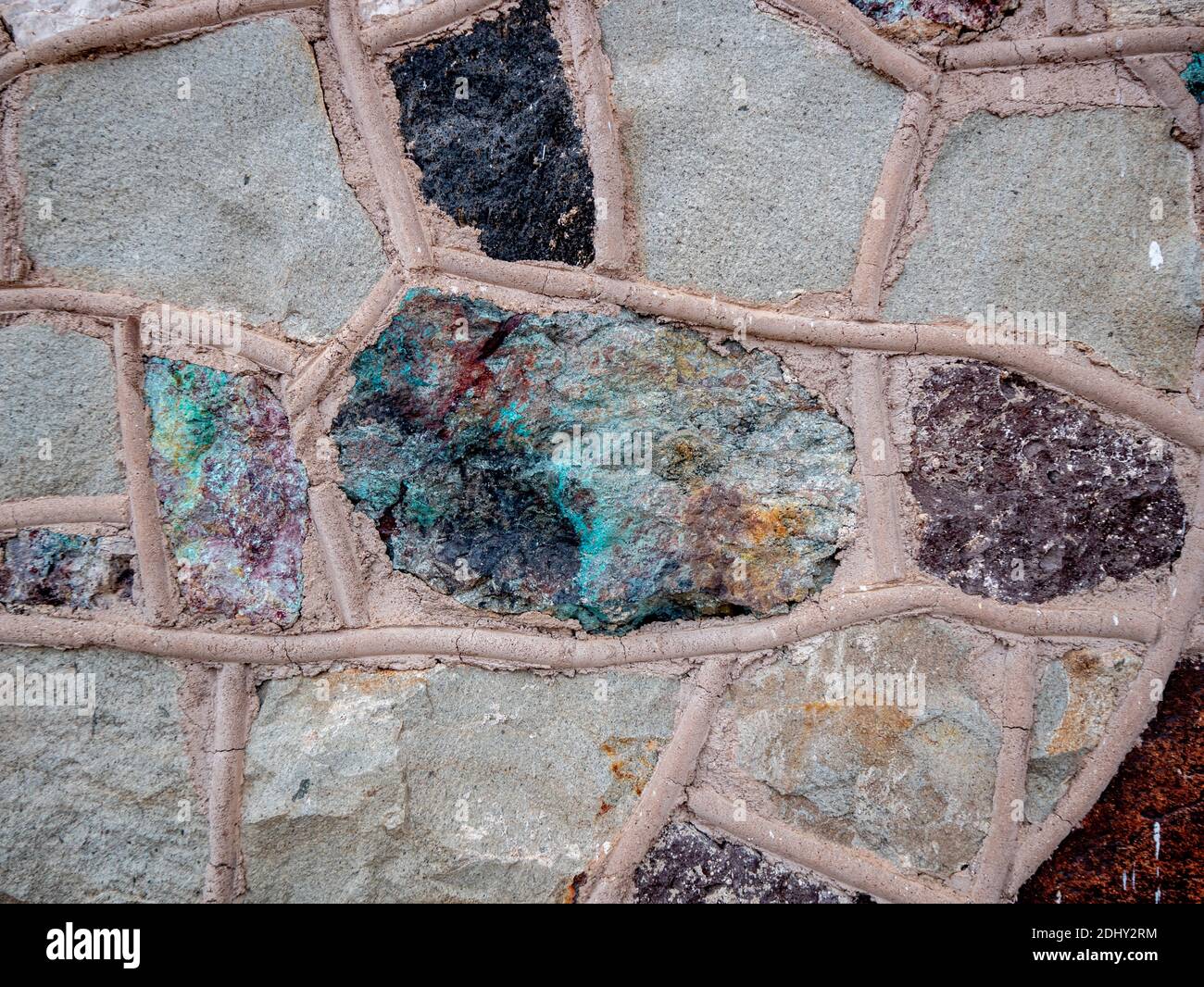 Farbenfrohe Mineralien in Natursteinwand mit dickem abgerundetem Fugenrost Stockfoto