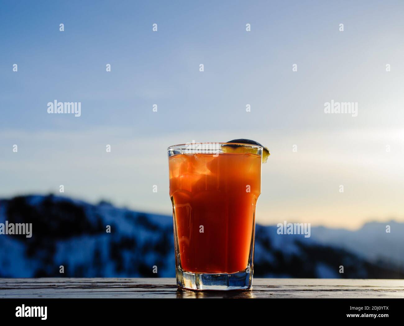 Beleuchtetes Glas mit orangefarbenem Cocktail-Drink mit Limettenkeil gegen verschwommene Berge. Stockfoto