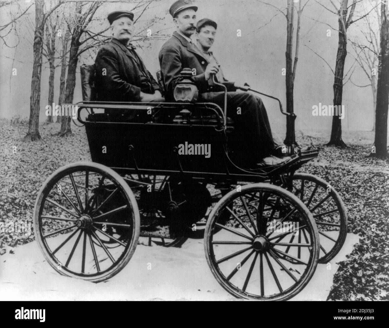 Das erste Oldsmobile - Foto zeigt drei Männer, die in einem Auto in einem waldähnlichen Bereich sitzen; Automobil sitzt auf Stoff auf einem mit Blättern bedeckten Boden, 1897 Stockfoto