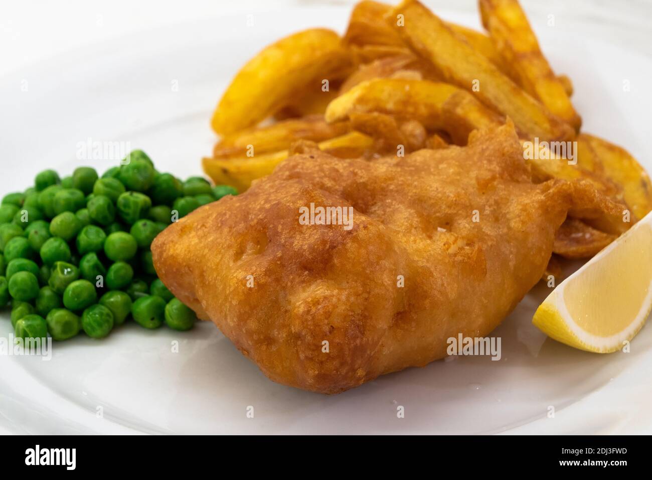 Fisch und Chips mit Erbsen und Zitrone auf einem weißen Teller Close Up, ein traditionelles Gericht der britischen oder englischen Küche Stockfoto