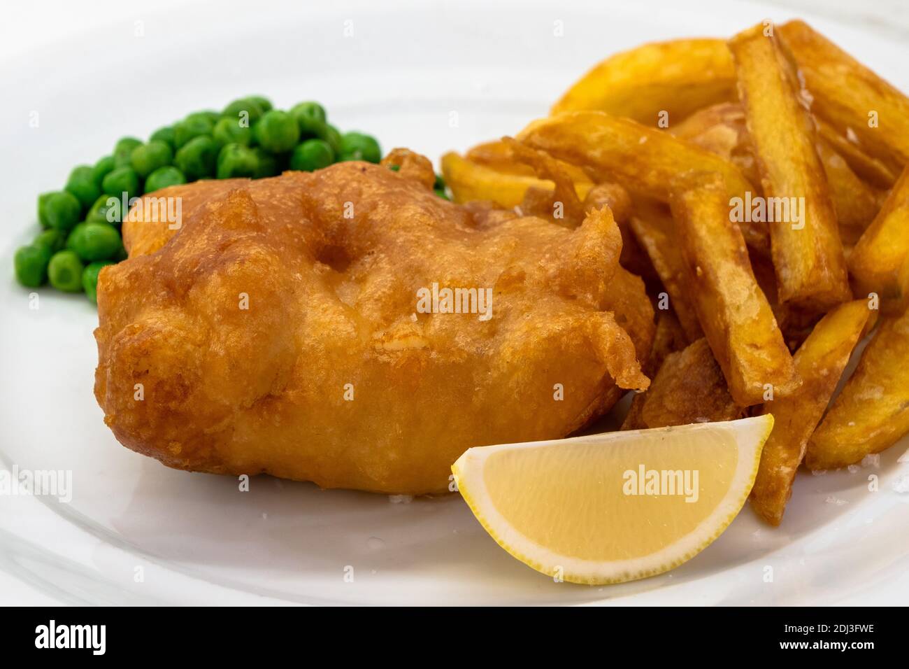 Fisch und Chips mit Erbsen und Zitrone auf einem weißen Teller Close Up, ein traditionelles Gericht der britischen oder englischen Küche Stockfoto