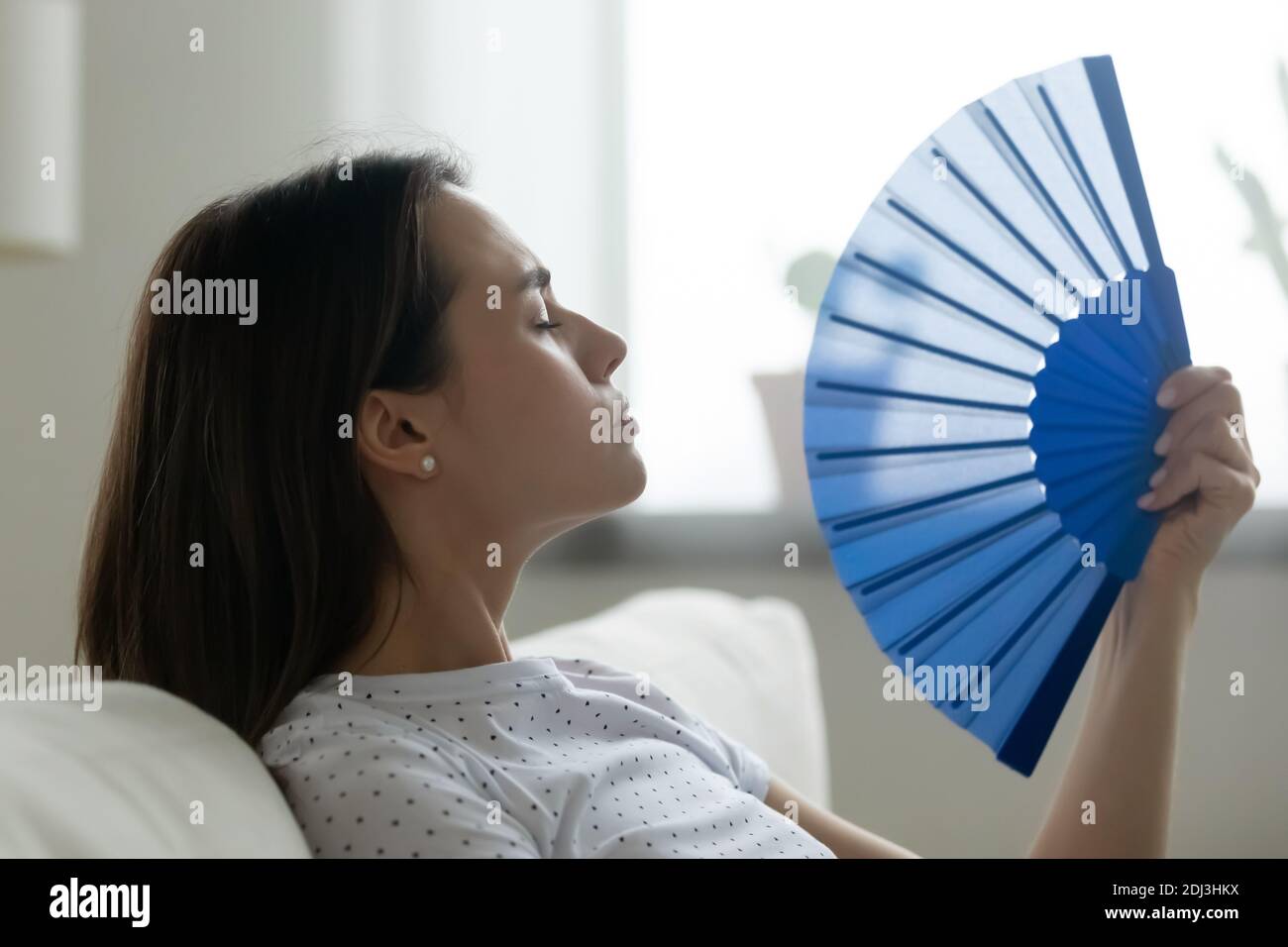Nahaufnahme überhitzte junge Frau winkt blauen Papierventilator Stockfoto