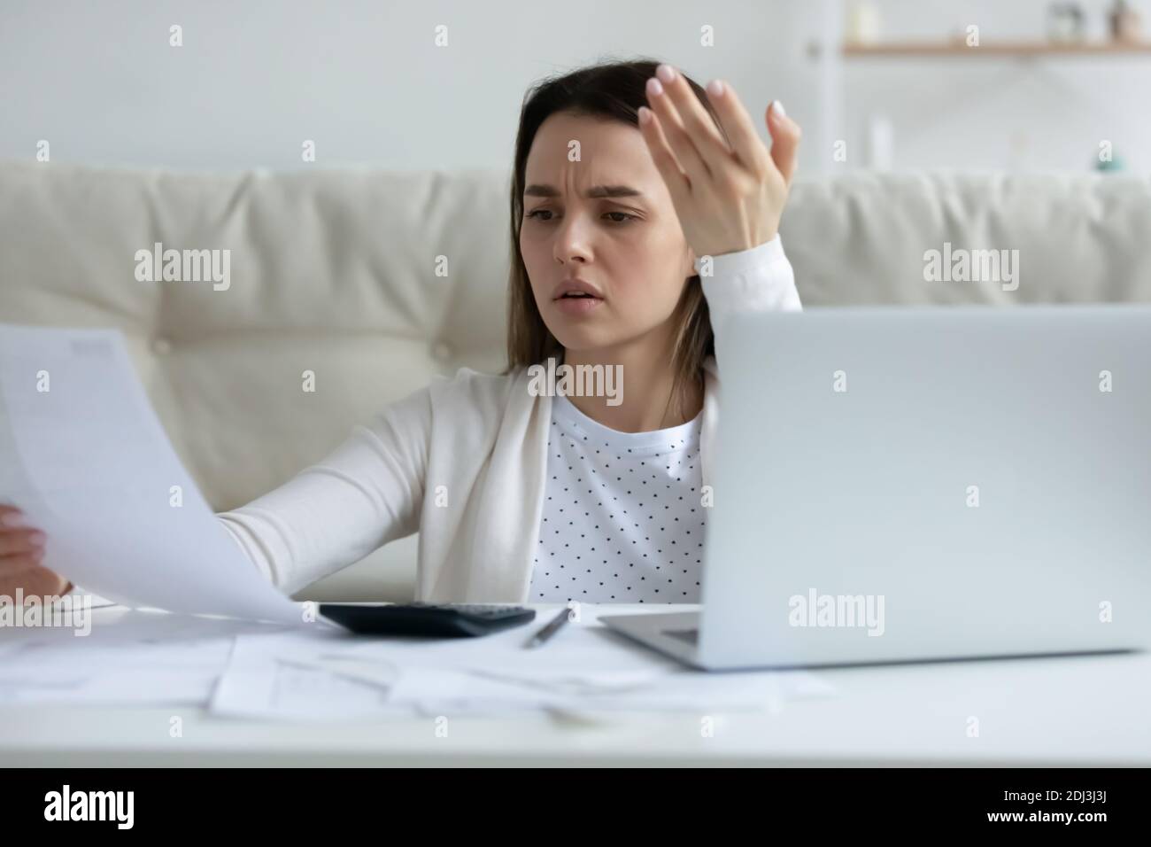Irritierte junge Frau prüft finanzielle Dokumente, mit Laptop Stockfoto