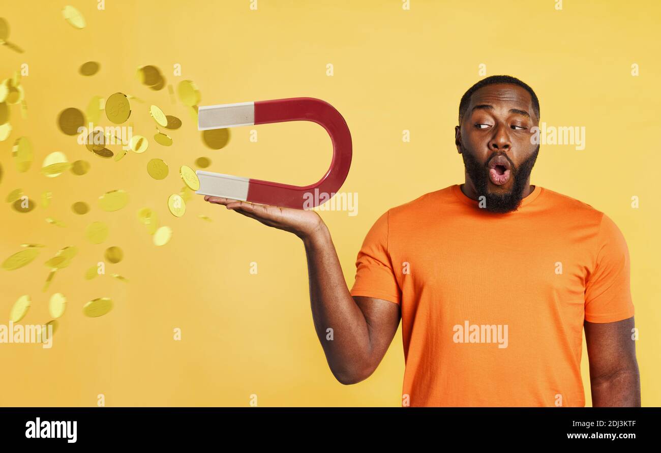 Überrascht schwarzen Mann hält einen großen Magneten, der Geld fängt. Gelber Hintergrund Stockfoto